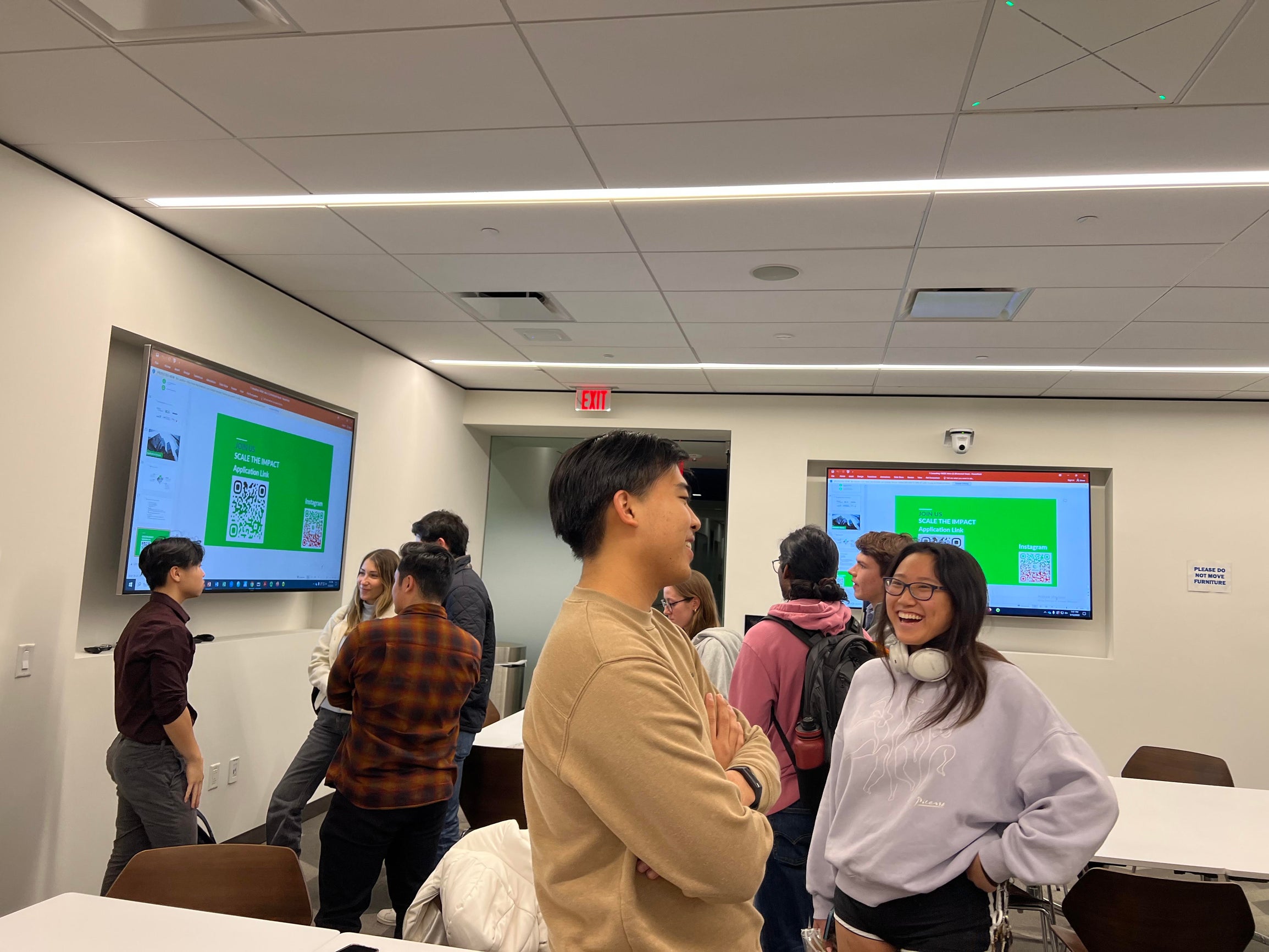 Students standing in a classroom talking to one another.