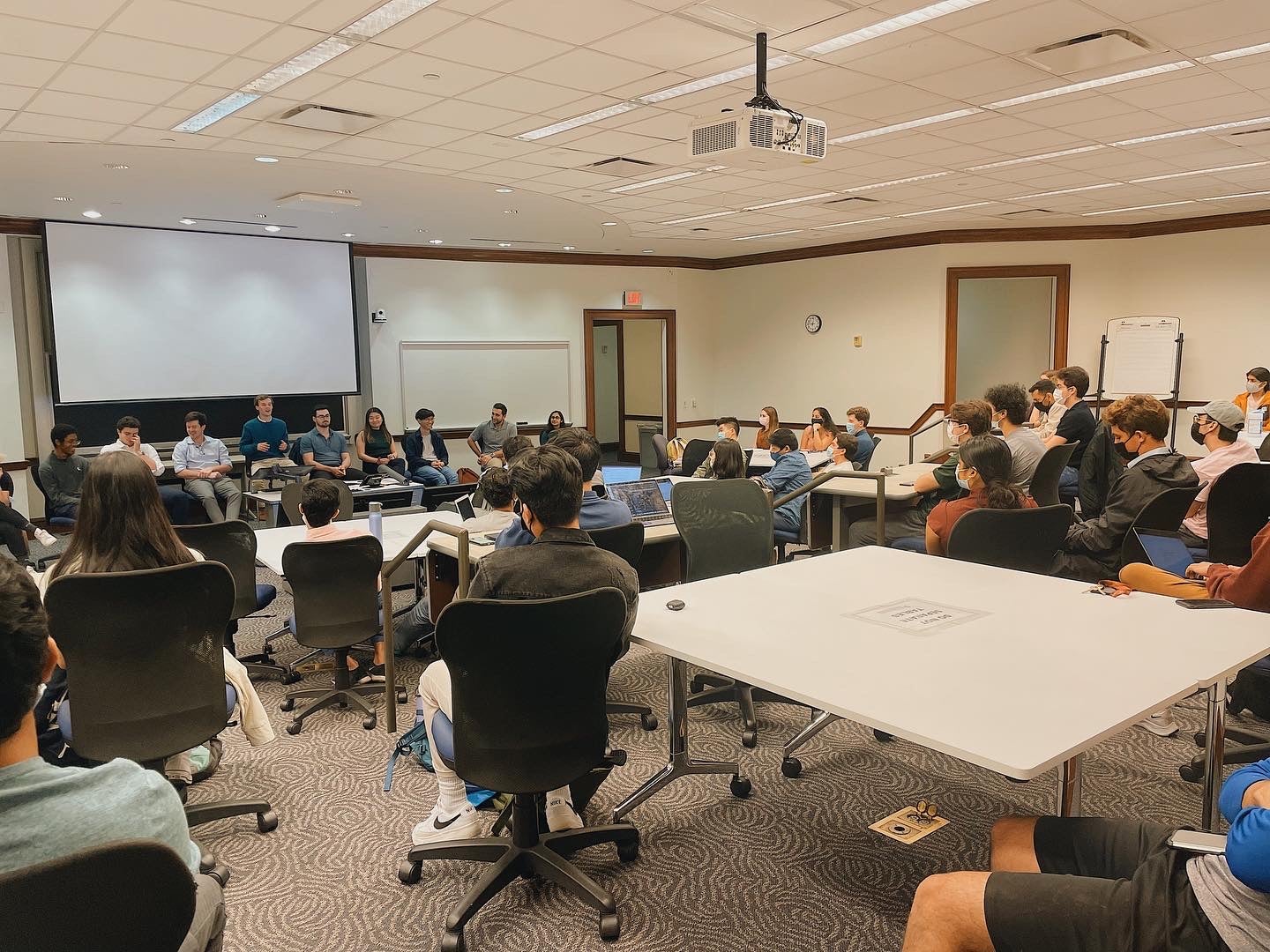 Students in a classroom, sitting down while listening to speakers working in finance.