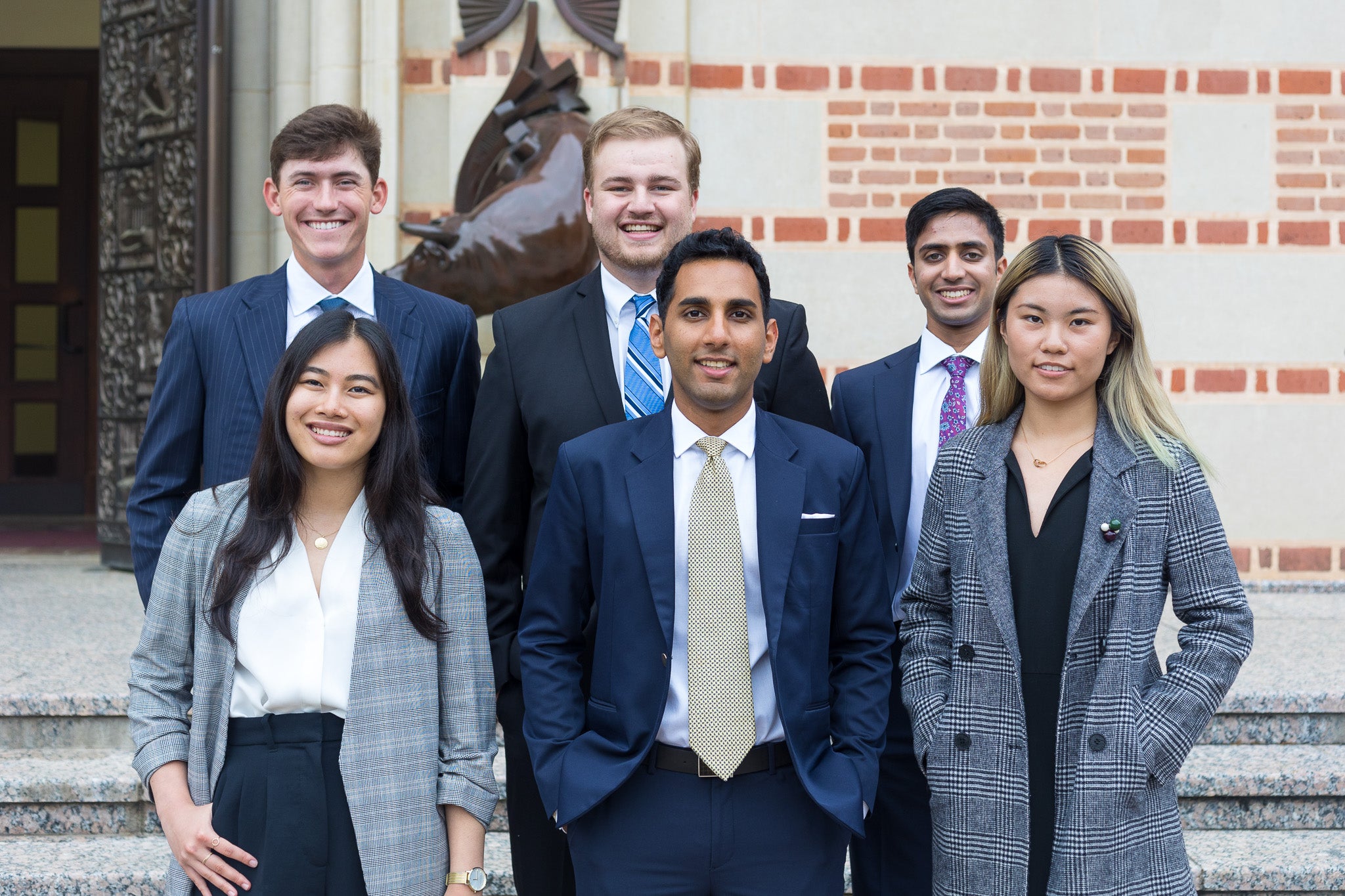 6 students standing in three-person rows, wearing business formal outfits.