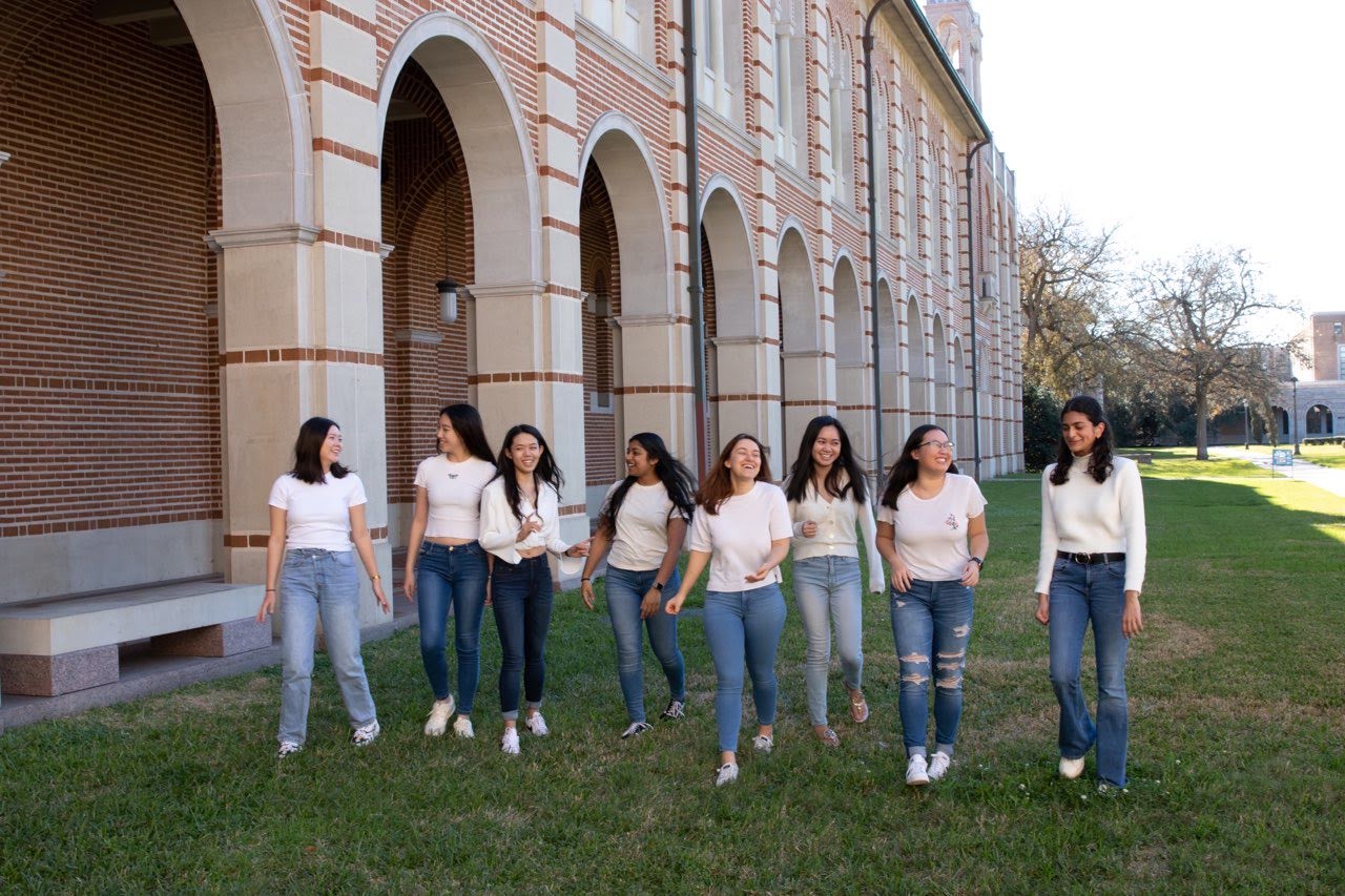 A group of female students standing in grass, candidly laughing.