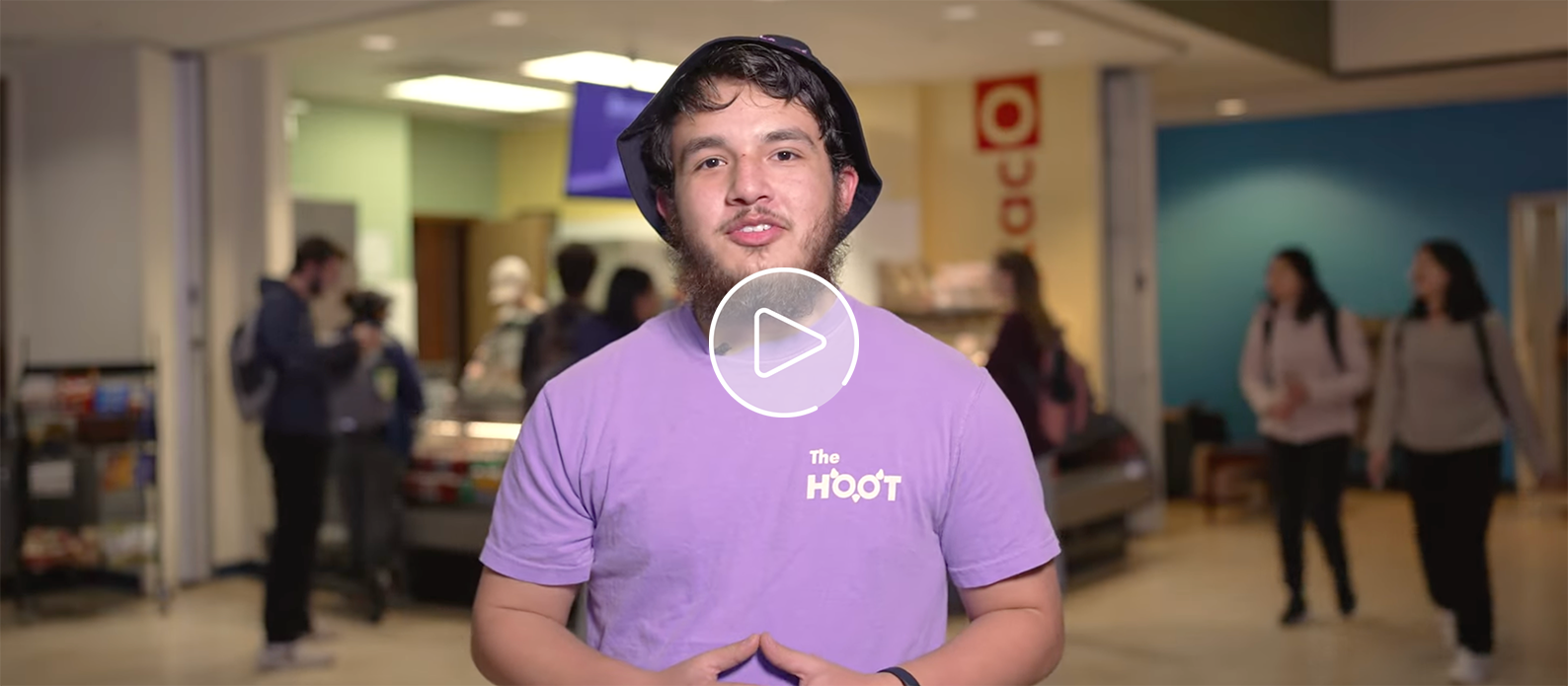 Male student wearing lilac T-Shirt with the words "The Hoot" written on his upper left chest.