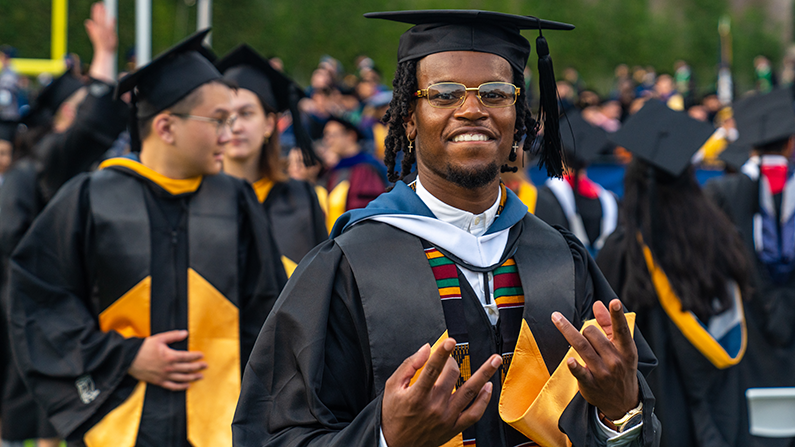Male student wearing full graduation regalia set smiling at camera.