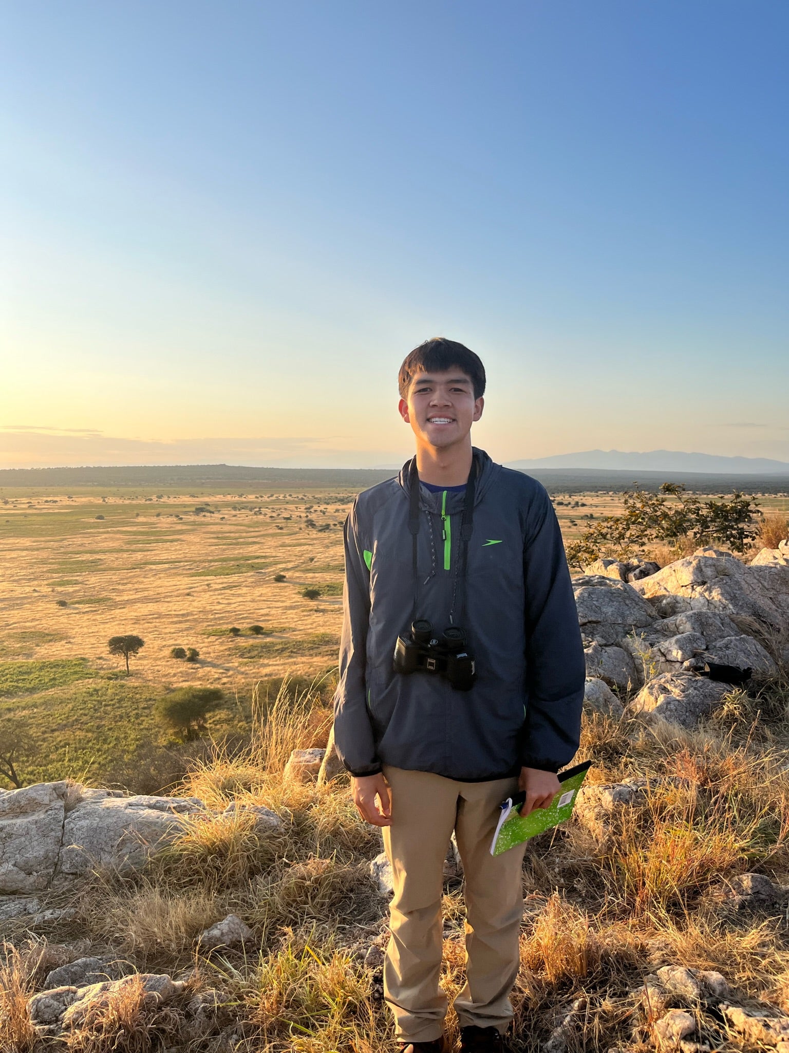 A college student wearing a jacket and pants, standing in grass in the Savannah 