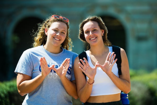 2 students posing for a picture and making owl wings with their hands 