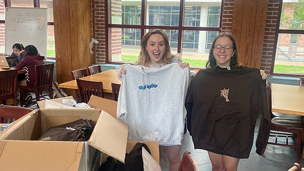 2 female college students posing while holding up sweatshirts