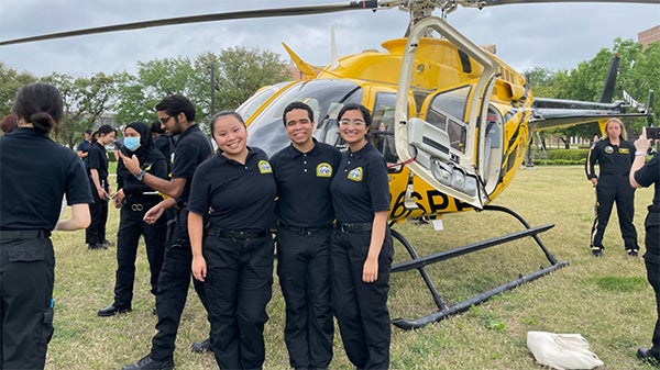3 college students posing in front of a helicopter