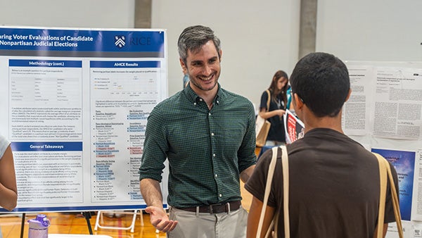 A professor shows a student, whose back faces the camera, a social sciences research report at an academic fair