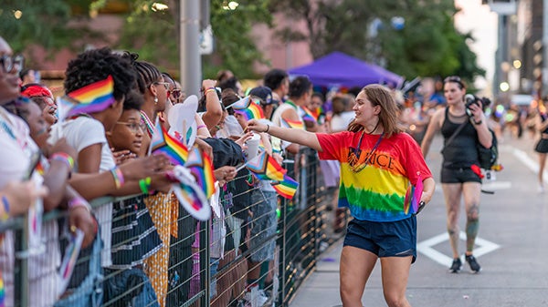 A girl in a rainbow-patterned Rice shirt engages with visitors at a pride parade