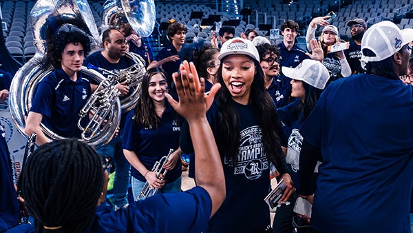 A girl gives another person a high-five at a sporting event; people surrounding them wear their Rice blue spirit wear