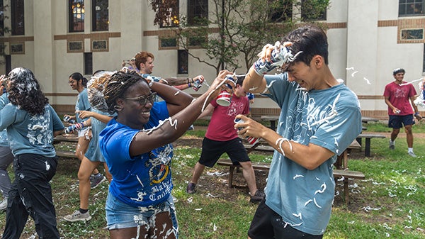 Two students spray each other with cool whip in a lighthearted outdoor activity