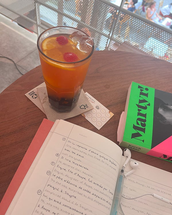A table with a drink, a book titled "Martyr", a journal with line-by-line French-to-English translations