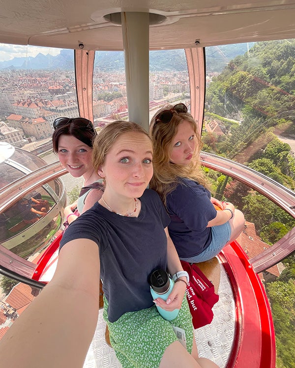 Blog writer Alysa and two friends on the top of a Ferris wheel, with the French nature and homes visible below