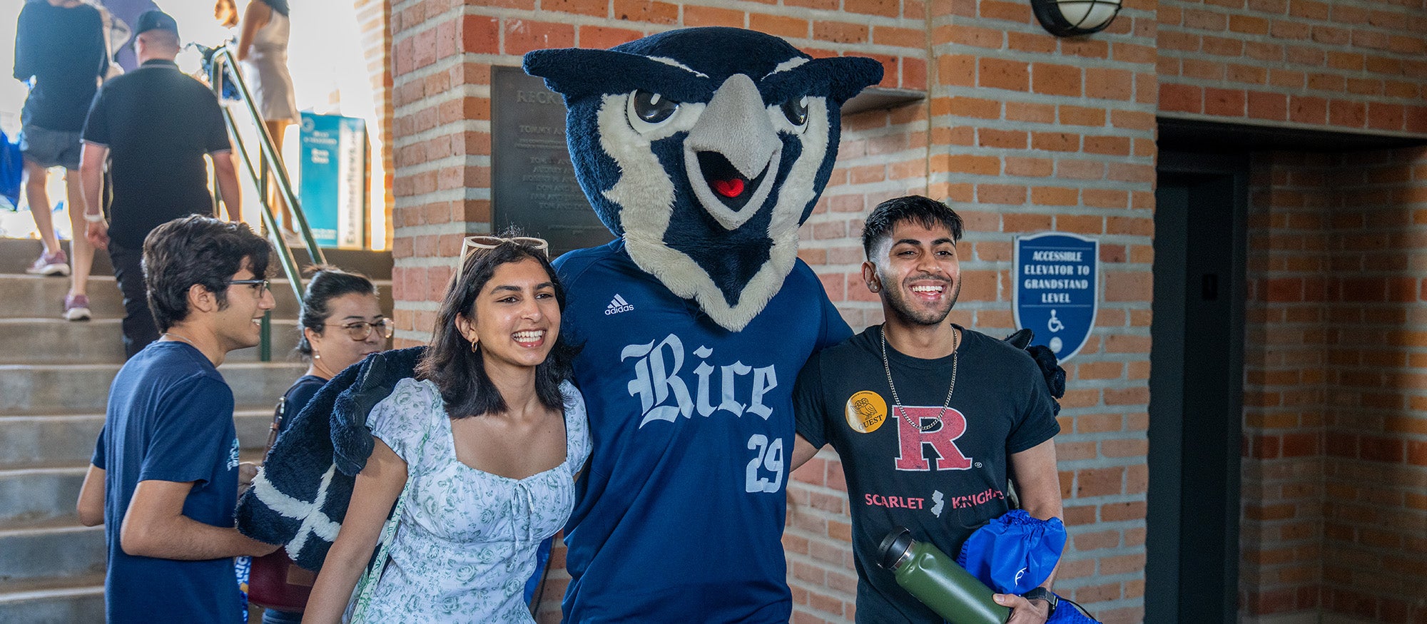 Two Rice students pose with a Rice University Owl mascot in '29 jersey, signifying their prospective graduating year