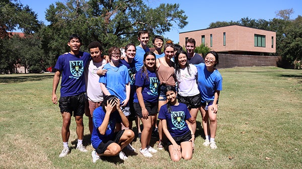 A group of Rice University students pose together outside in matching blue shirts