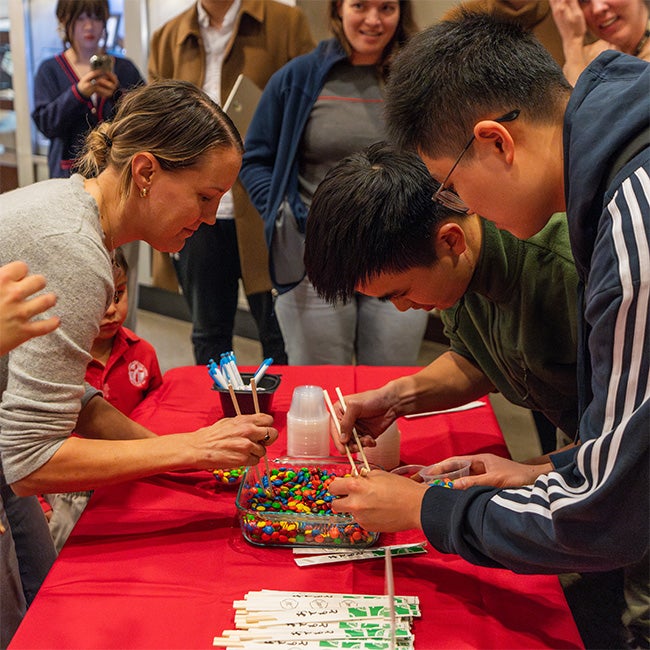 Students pick up candy from a glass dish using chopsticks