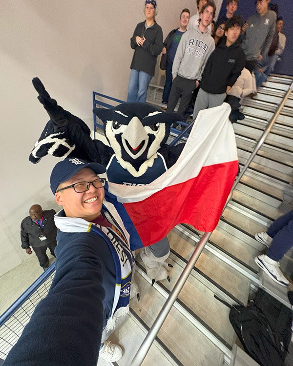 Hong Lin taking a selfie with the Owl mascot, holding up a Rice-themed Texas flag
