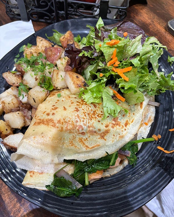 A plate of food with crepes, salad, and potatoes