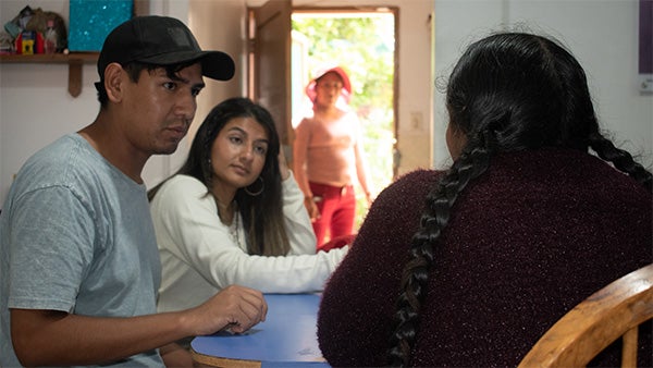 Side profile of a girl and a man at a table, watching a woman whose back faces the camera