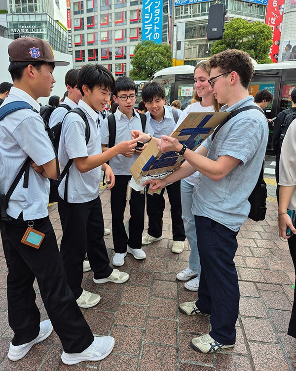 Japanese high schoolers in uniforms look at a poster board held by two others on a street