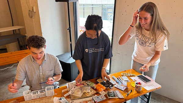 Three students working on a desk with many materials