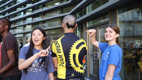 Two girls pointing up at the back of a man's head, shaved to have a W at the bottom