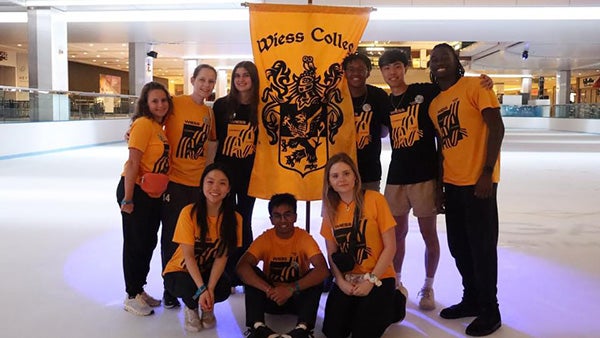 Several students in matching yellow T-shirts, holding a "Weiss College" banner on an ice rink