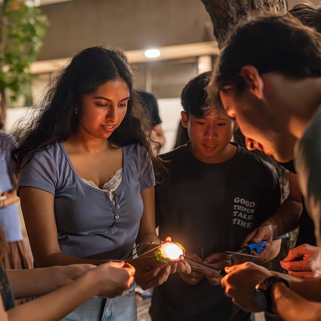 Many people lighting sparklers using a small lamp held by a girl