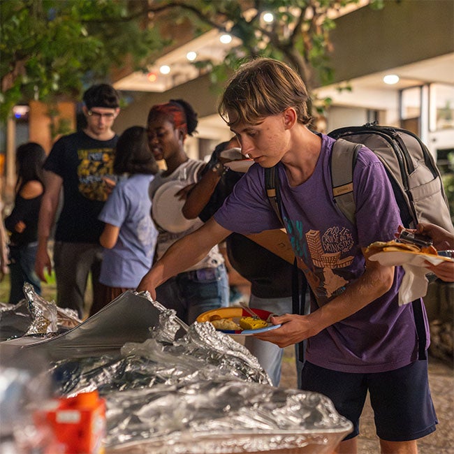 A male student gets food from foil bins