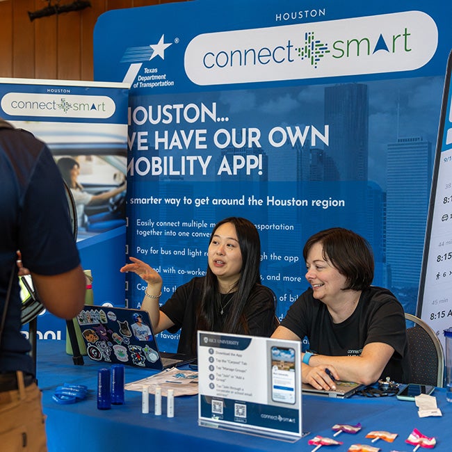 Two ladies sitting at a booth, a large blue poster behind them