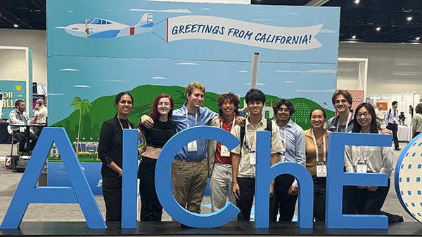 Several people standing behind life-size letters spelling "AIChE"