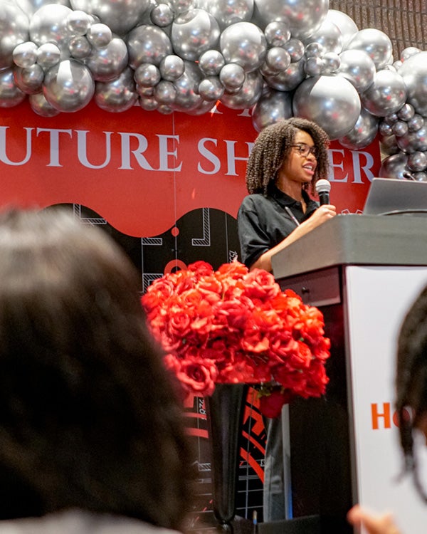 Partially obstructed person watching girl speaking behind a podium