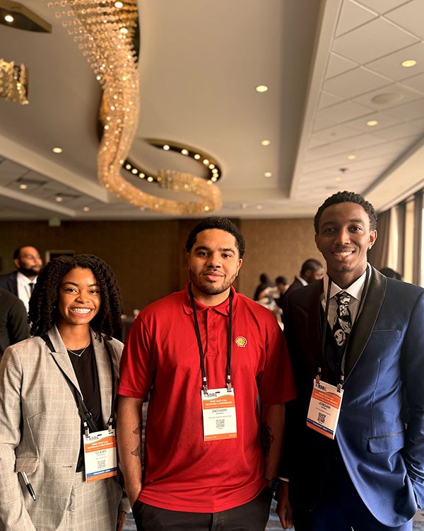 Three people with ID tags posing in a conference room