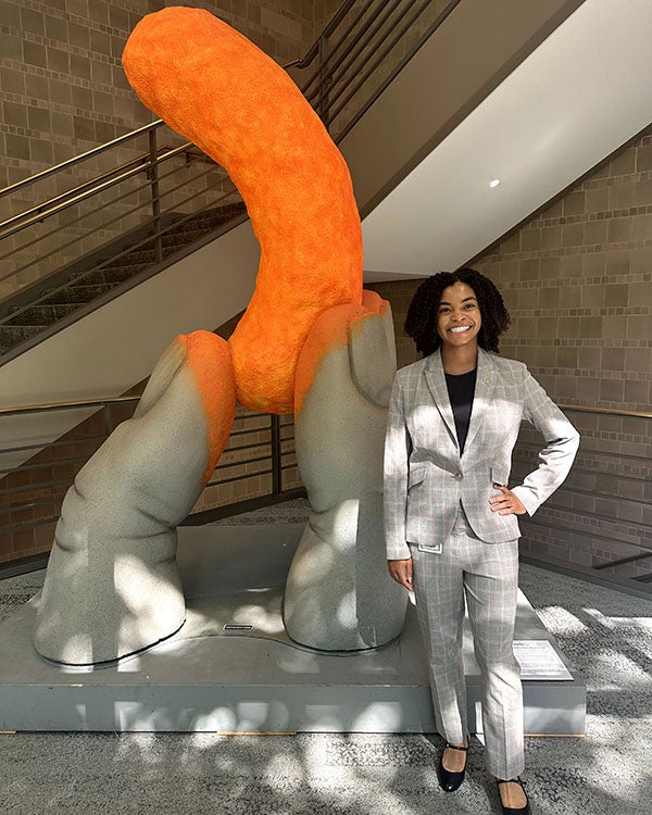 Girl posing in front of large hands holding a cheeto
