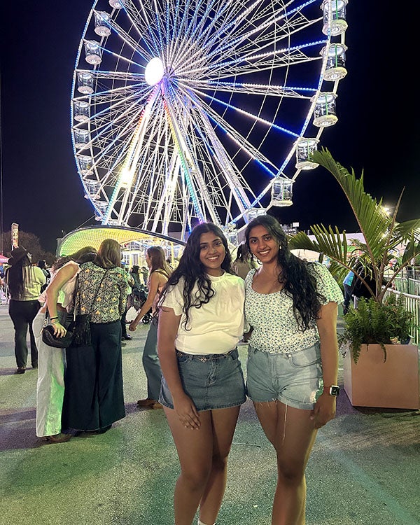 Two girls posed in front of a ferris wheel