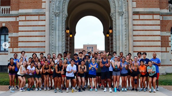 Large group of people in activewear standing in front of building with massive arch 