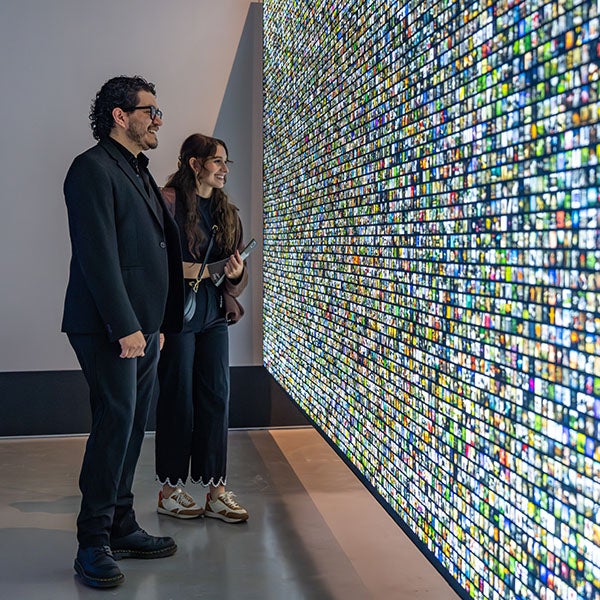 Two people look at wall of tiny, backlit square images