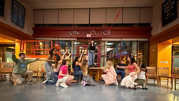 People gesturing at a sign that spells "JONES COLLEGE" 