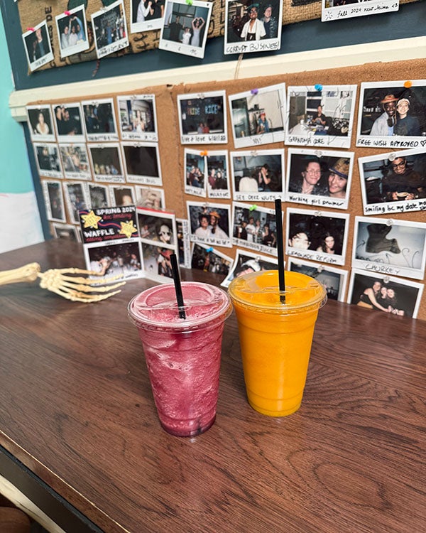 Two colorful drinks on a table, polaroids hung on the back wall