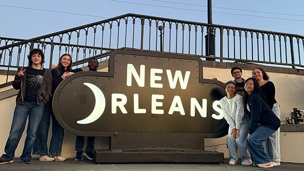 Three students next to a sign that says, "NEW ORLEANS" with the O taking the shape of a crescent moon