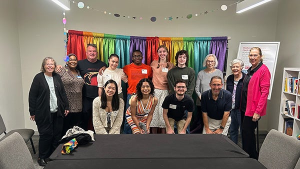 People stand or sit in front of a rainbow-colored backdrop