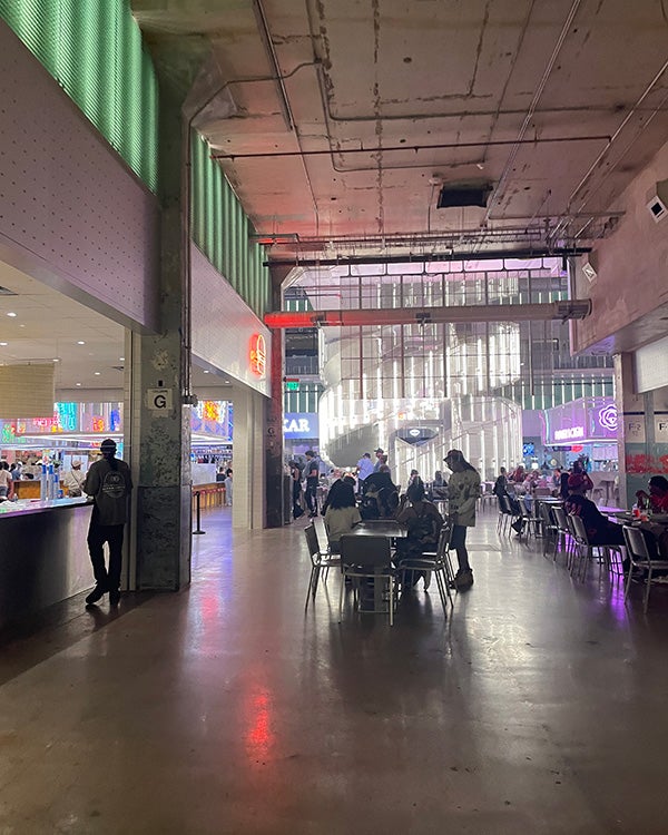 Hallway leading to open room with chairs & tables and neon and natural lighting