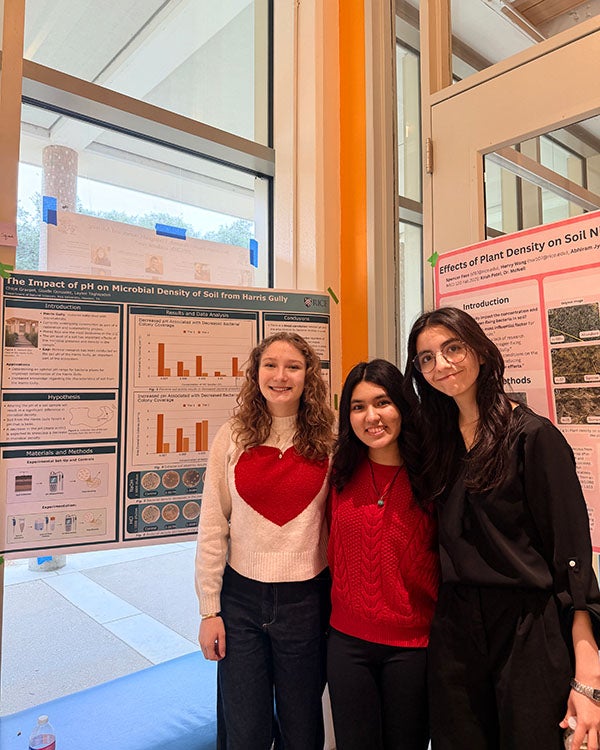 Three girls standing in front of a research poster