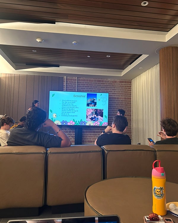 People presenting in front of TV; people watching sitting on sofa