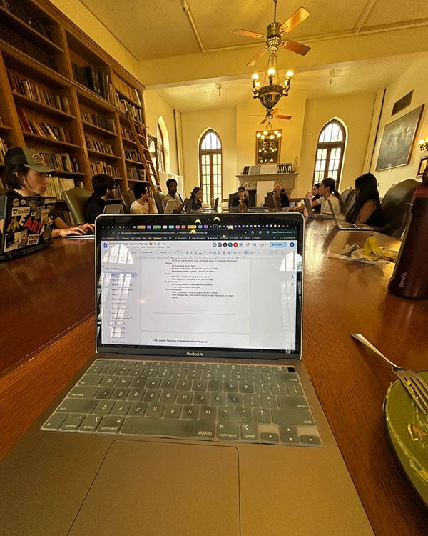 A laptop on a table, people sitting in a circle behind the laptop