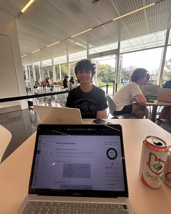 Laptop, a male student behind it, looking at the camera