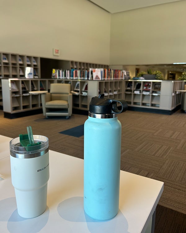 Two water bottles on a table in a carpeted room with bookshelves