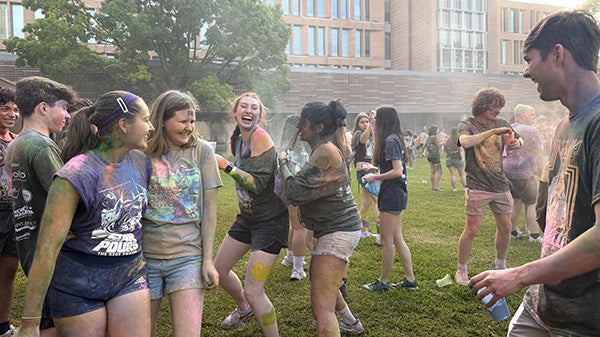 people in grass field playing with colored powders
