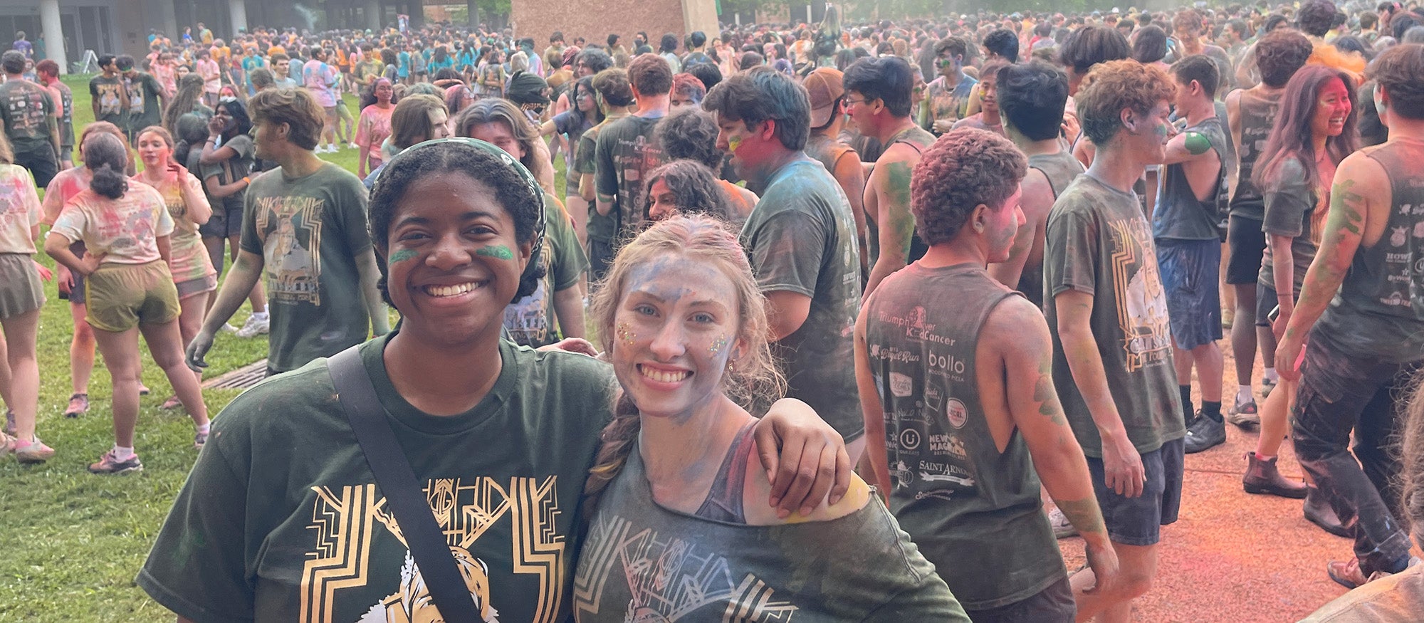 two people hugging, large crowds of people behind them; everyone in colored powders