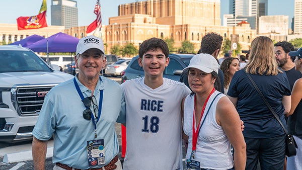 Three people standing together in a crowded area; a building visible in the back