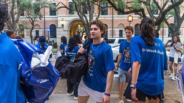 A crowd of people in matching blue shirts that say "O-Week Staff" on the back